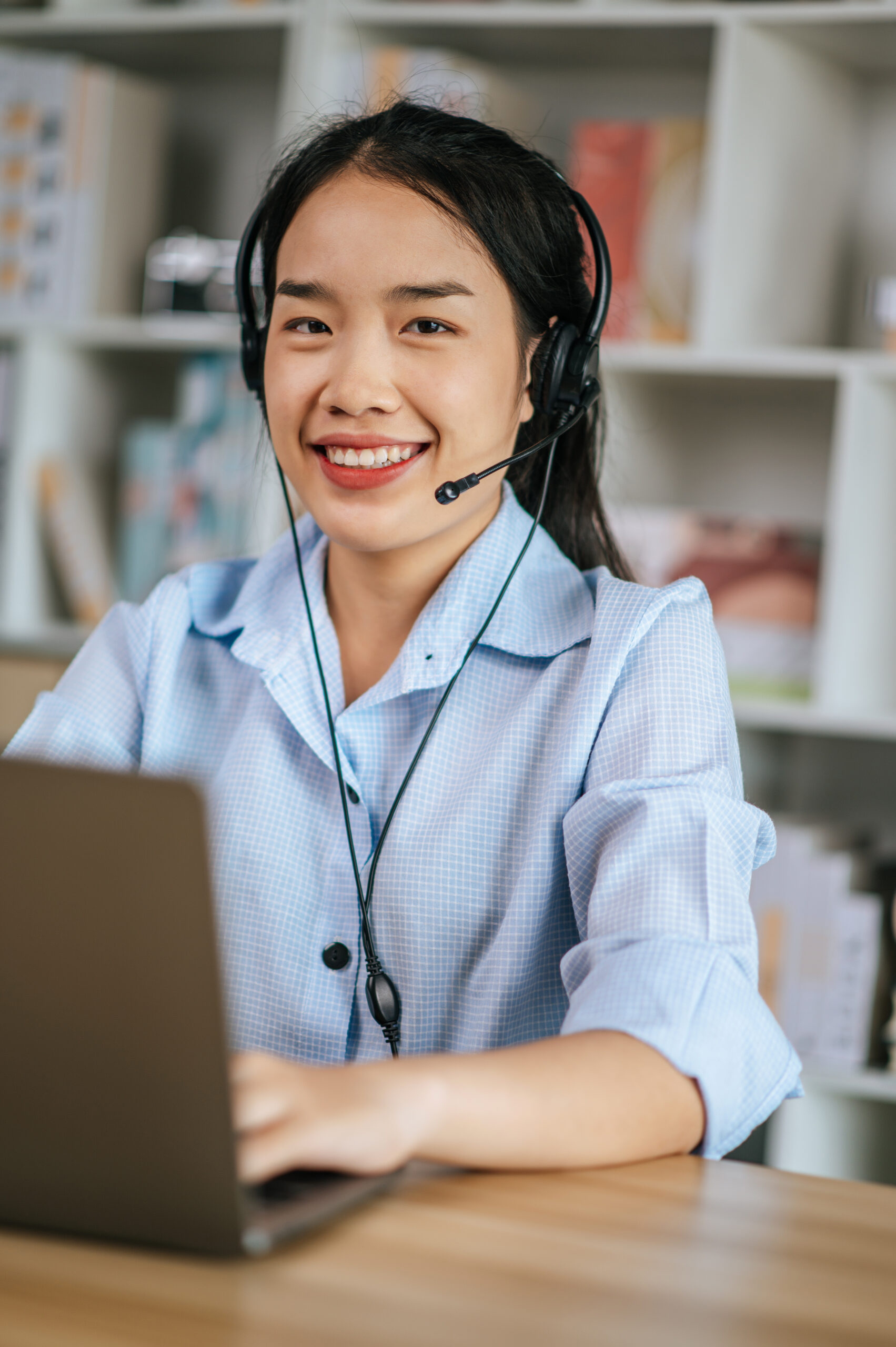 Cheerful Asian woman wear headset smiling and use laptop video call stream conference to working online while during quarantine covid-19 self isolation at home, work from home concept
